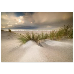 Foto strand Zeeland met helmgras in de voorgrond, een dynamische wolkenpartij en door regen gevormde texturen in het zand.