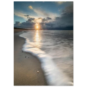 Foto strand Zeeland bij zonsondergang met een schelpje op de voorgrond, zonnestralen door de wolken en een vloeiende waterlijn.